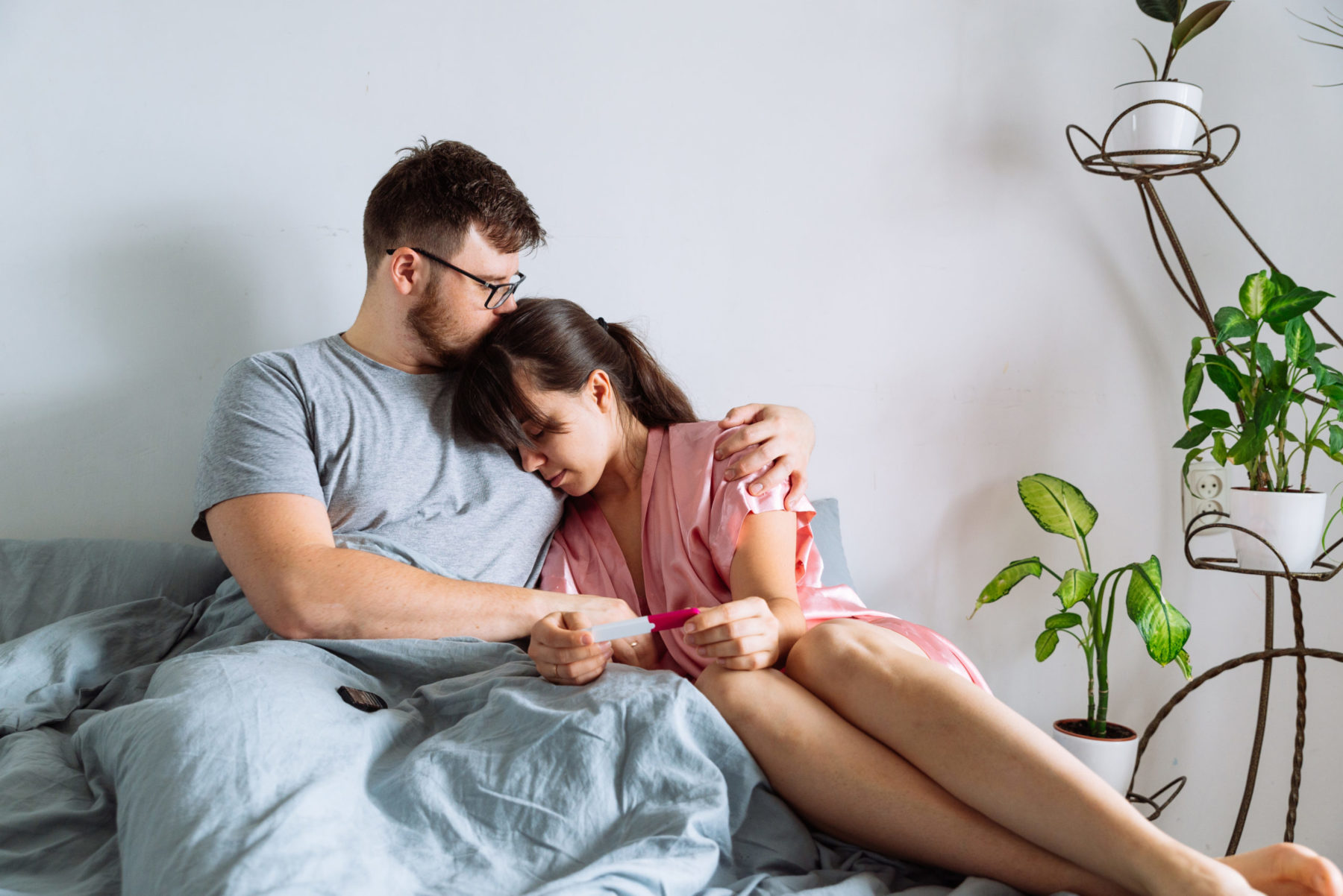 un couple assis sur un lit se réconforte d'un résultat négatif d'un test de grossesse