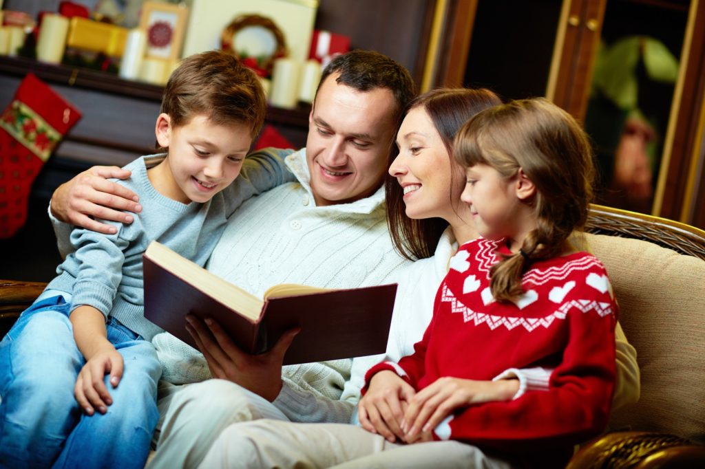 Un couple assis sur le canapé lit un livre avec ses enfants, un garçon et une fille