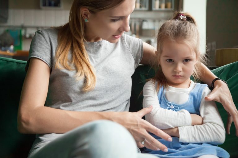 Une fille assise à côté de sa mère semble bouder, les bras croisés