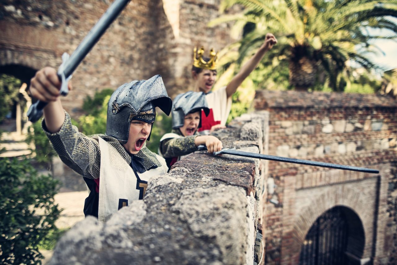 Deux enfants en tenue de chevaliers avec un casque et une épée à la main jouent en extérieur