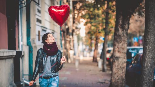 Une femme seule dans la rue tient regarde un ballon en forme de cœur rouge