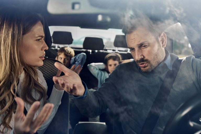 Une femme et un homme se dispute dans une voiture, les enfants derrière se bouchent les oreilles
