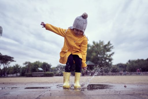 Une enfant avec des bottes saute dans une flaque d'eau