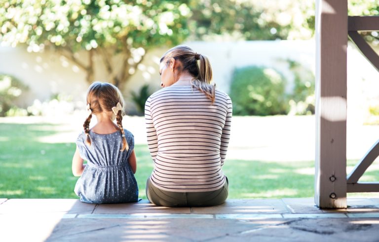 De dos, une maman discute avec sa fille assise sur le bord de la terrasse en bois